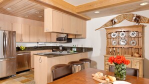 A kitchen with wooden cabinets, a stainless steel refrigerator, a microwave, and a dining area with a wooden table and chairs. - 700 Ute Apartment #703 4 Bedroom Home (Aspen)