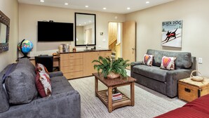 A modern living room with a grey sofa, a coffee table with a plant, a grey couch with patterned cushions, a wooden side table, a flat-screen TV mounted on the wall, a wooden cabinet, and a framed picture of a black dog. - 700 Ute Apartment #703 4 Bedroom Home (Aspen)