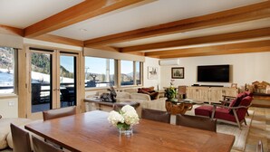 A spacious living area with a wooden dining table, comfortable seating, a television, and a view of the outdoors. - 700 Ute Apartment #703 4 Bedroom Home (Aspen)