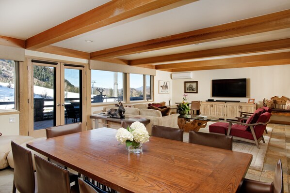 A spacious living area with a wooden dining table, comfortable seating, a television, and a view of the outdoors. - 700 Ute Apartment #703 4 Bedroom Home (Aspen)