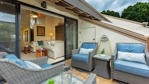 Un patio con mobiliario de mimbre, una puerta de cristal que da a un espacio interior y vista al cielo.