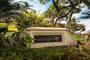 A sign for 'Maui Kamaole' with a tropical garden backdrop. - Maui Kamaole M207 2 Bedroom Condo (Kihei)