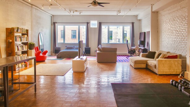 A spacious living area with a wooden floor, a sofa set, a coffee table, a bookshelf, and a flat-screen TV.