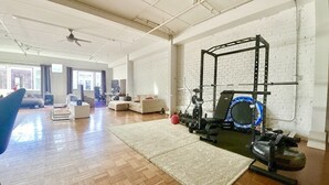 A spacious living area with a large exercise machine, a blue exercise disc, and a white brick wall.