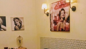 A room with a green sofa, a small table with a lamp, wall-mounted lights, and framed pictures on the wall.