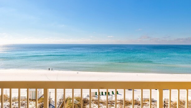 A beach view with a clear sky, a sandy shore, and a railing in the foreground. - Pelican Beach 0602 1 Bedroom Condo (Destin)