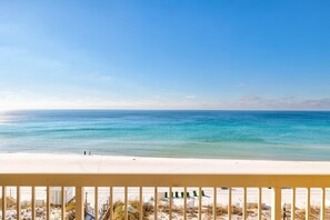 A beach view with a clear sky, a sandy shore, and a railing in the foreground. - Pelican Beach 0602 1 Bedroom Condo (Destin)
