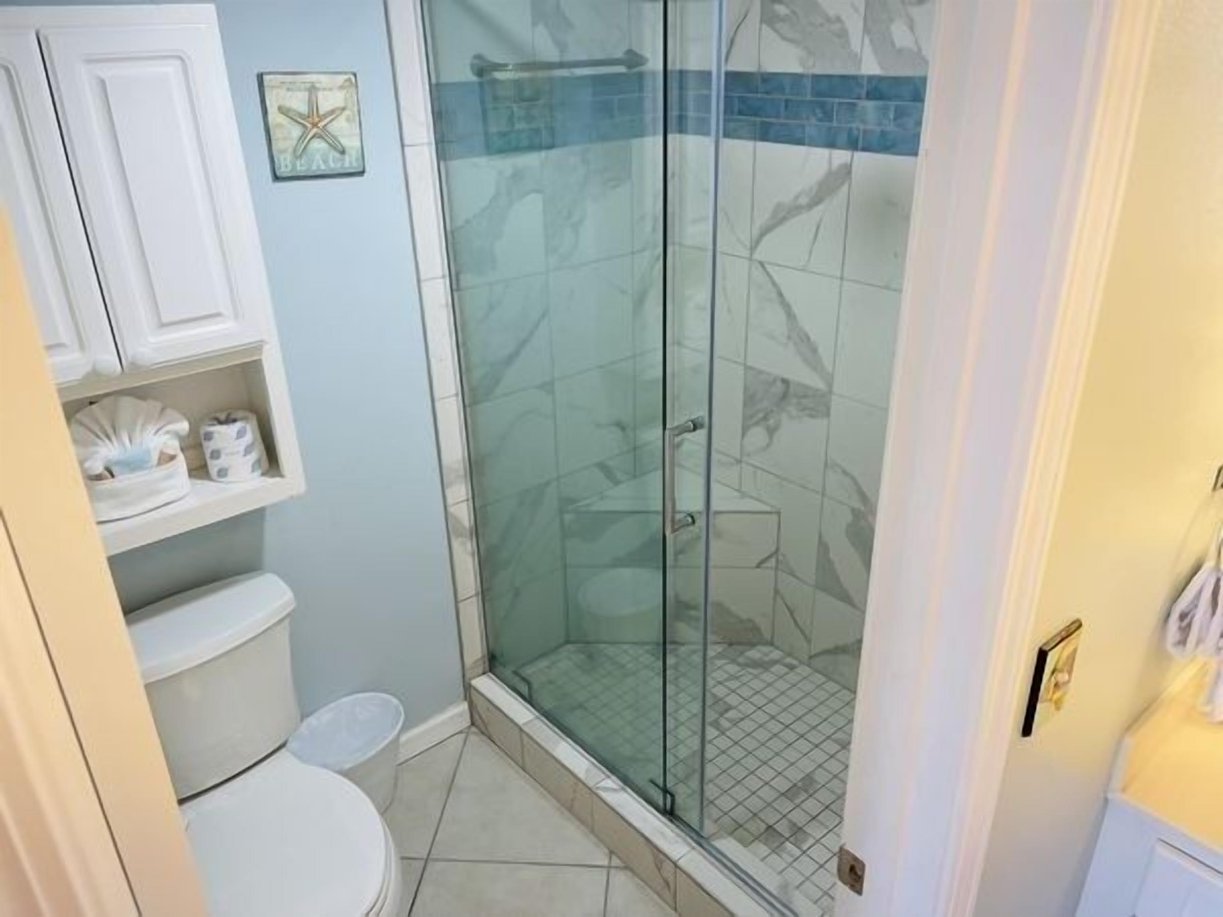 Een badkamer met een douchecabine van glas, een toilet en een plank met toiletartikelen.