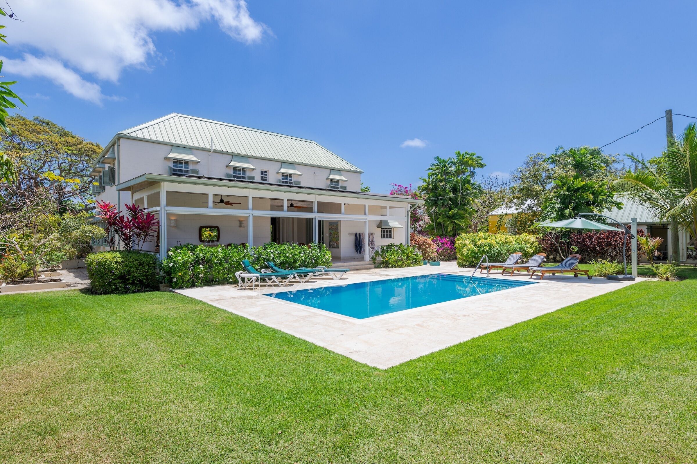 A two-story house with a swimming pool, surrounded by a well-maintained lawn and various plants.