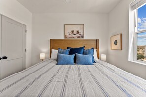 A bedroom with a large bed, a wooden headboard, two wall-mounted lamps, and a framed picture above the bed. - Periwinkle Sky 3 Bedroom Condo (St. George)