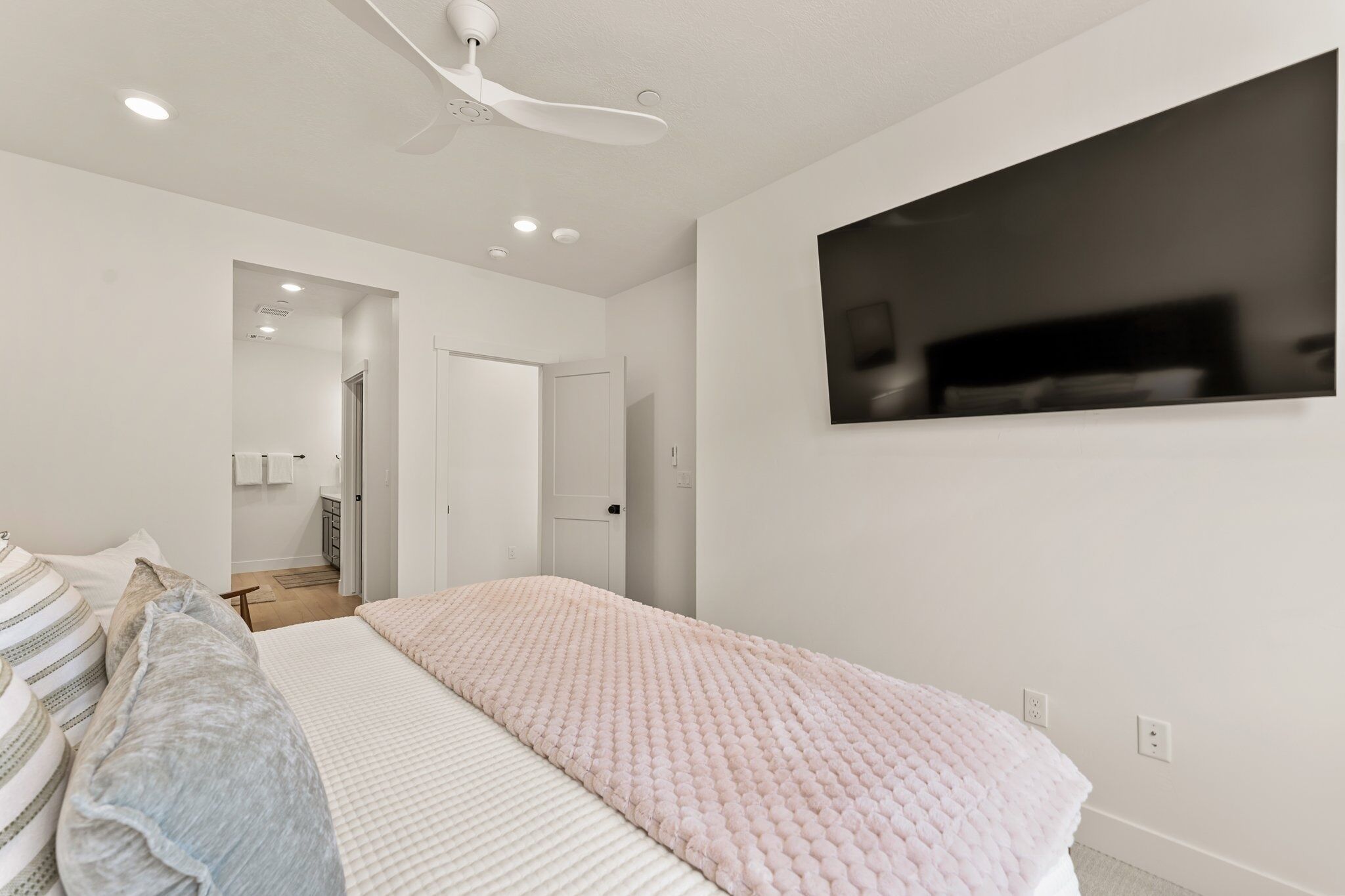Un dormitorio moderno con una cama grande, un ventilador de techo y un televisor montado.