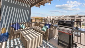 Ein Balkon mit Rattanmöbeln, einem Grill und einem gemusterten Boden.