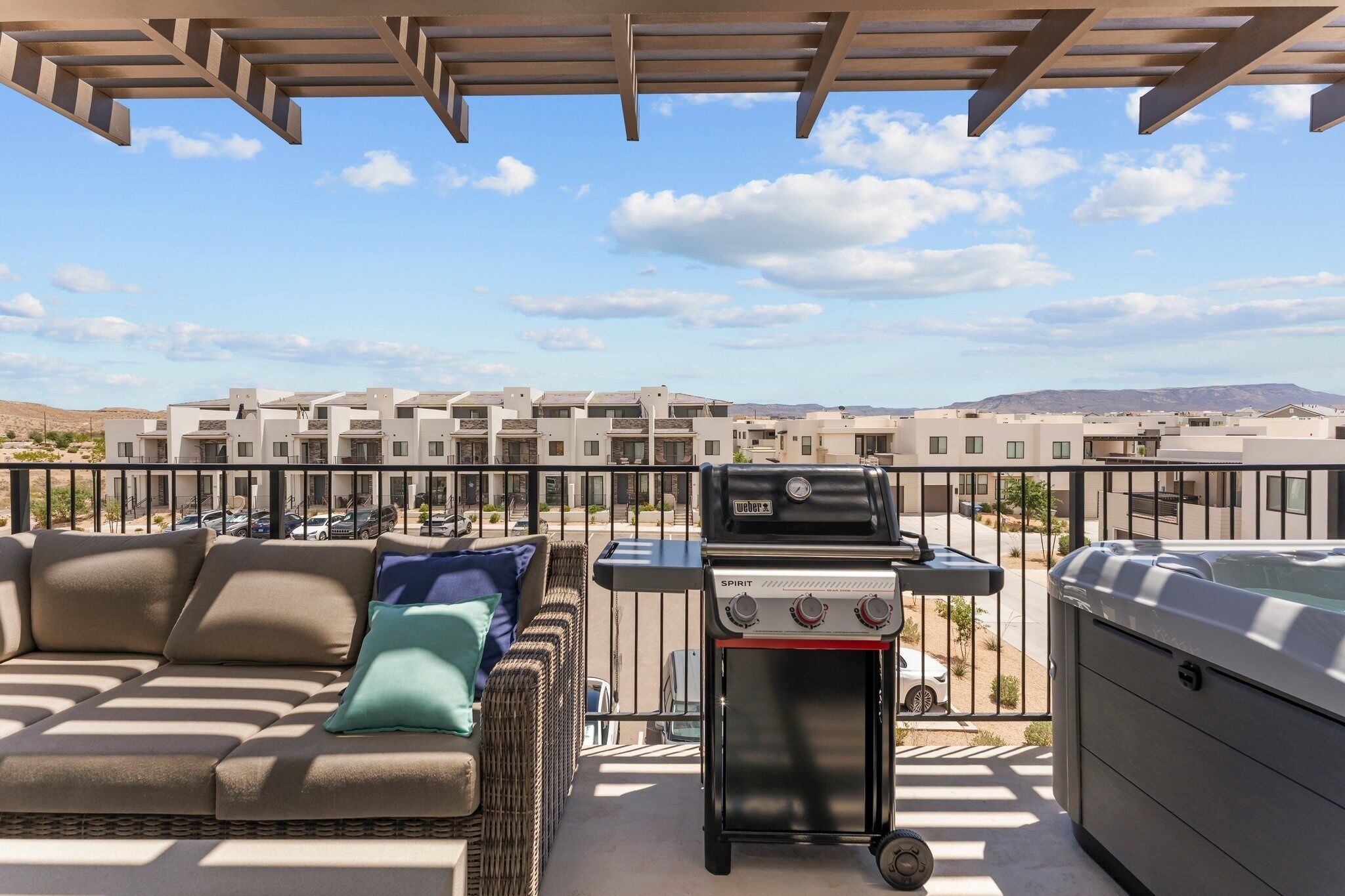 A balcony with a grill, a sofa with cushions, and a view of buildings in the background.