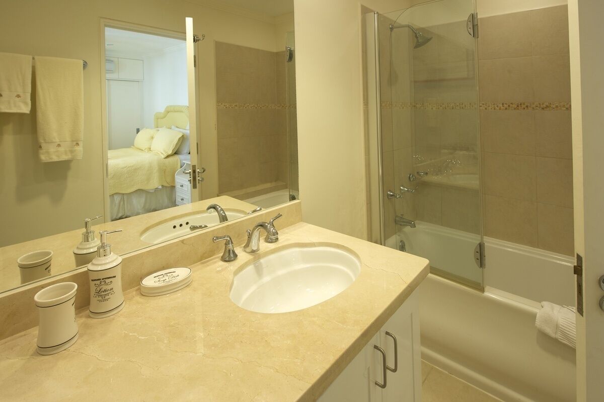 A bathroom with a sink, mirror, toiletries, and a glass-enclosed shower.