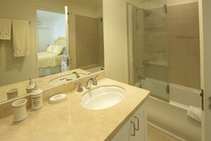Une salle de bain équipée d’un lavabo, d’un miroir, d’articles de toilette et d’une douche fermée par des parois en verre.