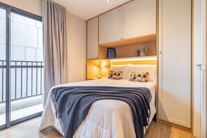 Ein Schlafzimmer mit einem Bett, einem Nachttisch, Vorhängen an einem Fenster und Blick auf einen Balkon.