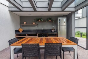 Eine moderne Küche mit einem Holztisch und Stühlen, eingebauten Regalen mit Pflanzen und einem Kühlschrank.