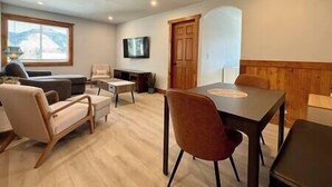 A modern living room with a sofa, chairs, a dining table, and a TV mounted on the wall.