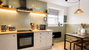 Una cocina moderna con horno integrado, microondas y tostadora. Hay una zona de comedor con mesa y sillas.