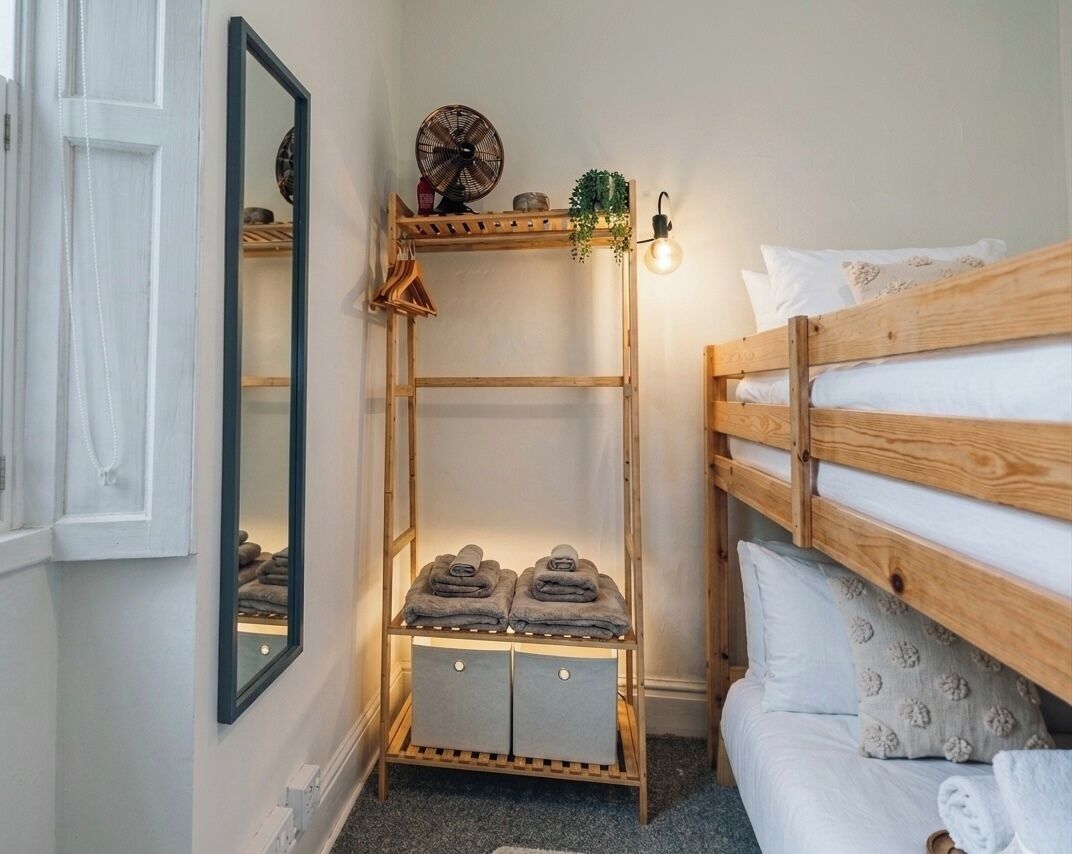 Ein Schlafzimmer mit einem Holzbett, das als Etagenbett genutzt wird, einem Regal mit Handtüchern, einem Spiegel und einem Wandventilator.