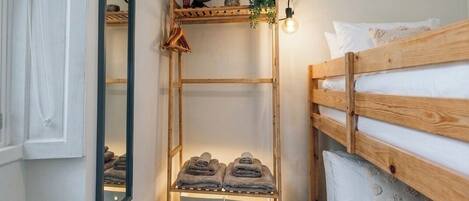 Ein Schlafzimmer mit einem Holzbett, das als Etagenbett genutzt wird, einem Regal mit Handtüchern, einem Spiegel und einem Wandventilator.