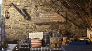 A rustic stone wall with a plaque, a wooden bench, and a sofa with cushions. - Dafne Konukevi (Bozcaada)