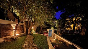 A stone pathway leading to a blue door with a wreath, surrounded by lush greenery and stone walls. - Dafne Konukevi (Bozcaada)