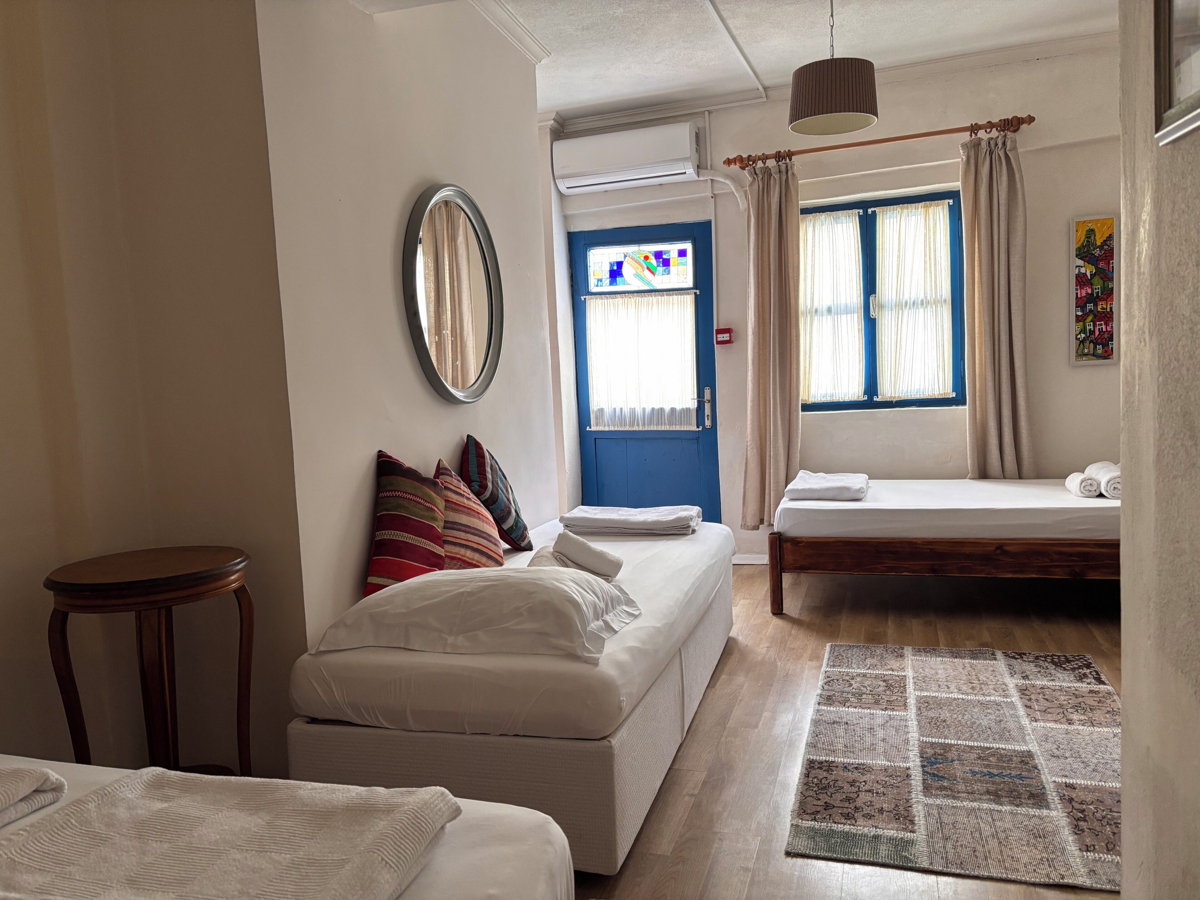 Ein Schlafzimmer mit einer Couch, einem Bett, einem kleinen Tisch, einem Spiegel und einem Fenster mit Vorhängen.
