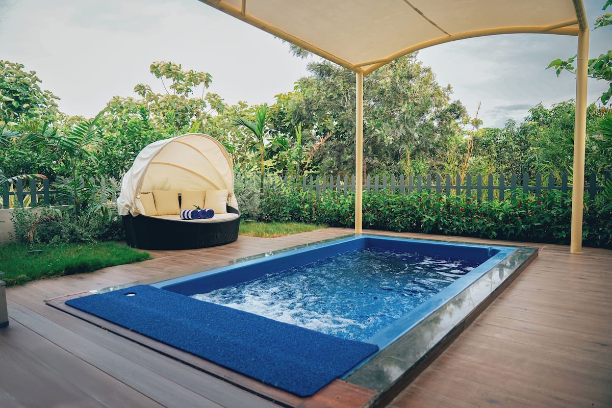 A hot tub under a canopy, surrounded by lush greenery and a wooden deck.