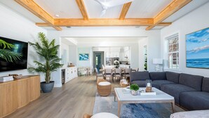 Een ruime woonkamer met een plafondventilator, een televisie, een eethoek en een keuken op de achtergrond.