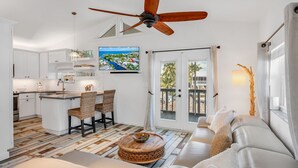A modern kitchen with white cabinets, a dining area with wicker chairs, a large wooden coffee table, and a ceiling fan.