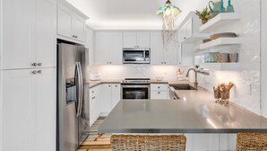A modern kitchen with white cabinetry, stainless steel appliances, a central island, and decorative items on shelves.