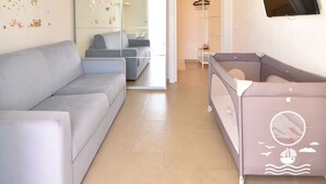 Un soggiorno moderno con un divano grigio, un recinto giochi per bambini, un grande lampadario e una TV a parete.