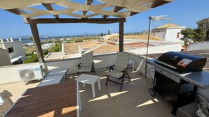 Una terrazza sul tetto con una pergola, due sedie, un barbecue e un tavolo.