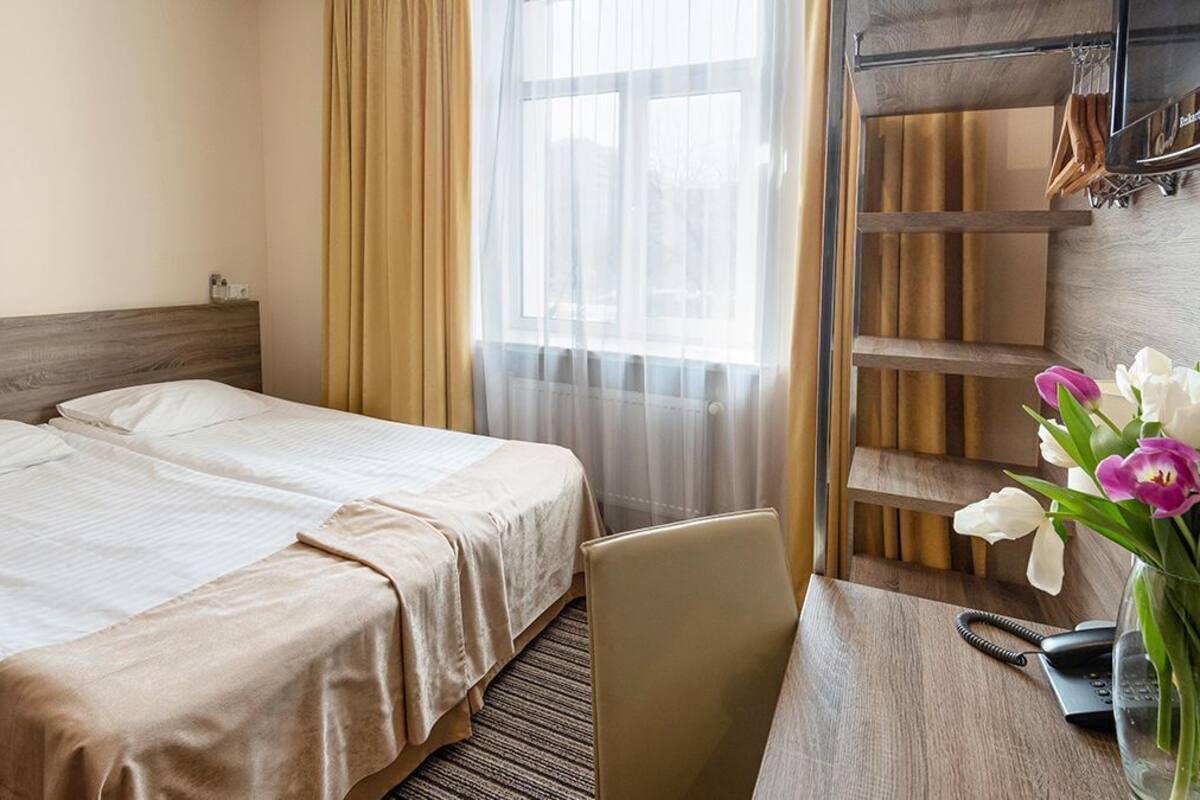 Habitación de hotel con dos camas, un escritorio con silla, un teléfono y un florero con flores.