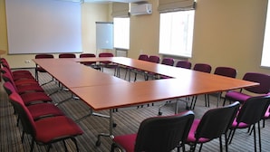 Une salle de conférence avec une longue table, des chaises rouges, un tableau blanc et un écran de projection.