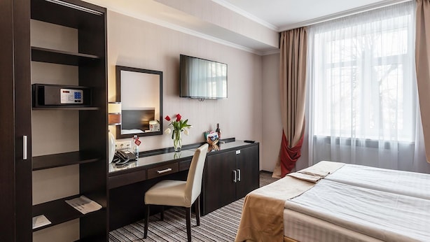 Une chambre d’hôtel comprenant un lit, un bureau avec une chaise, une télévision, un minibar et une fenêtre avec des rideaux.