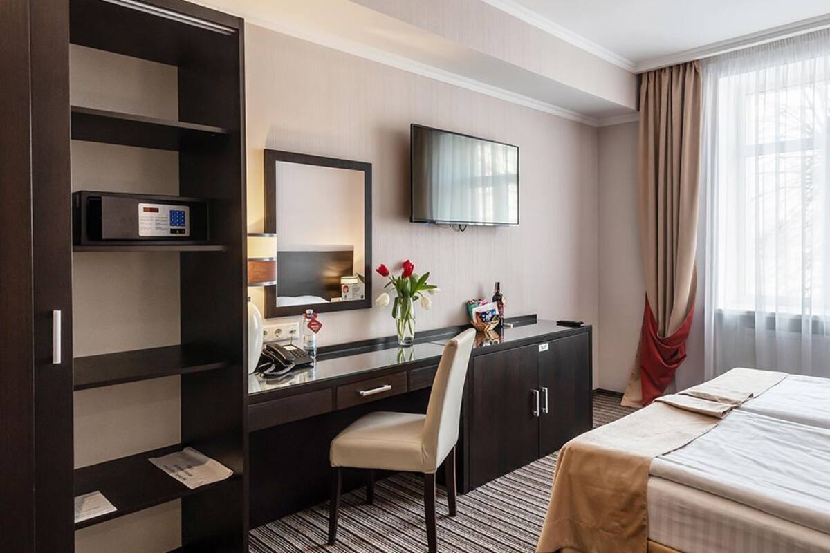 Una habitación de hotel con cama, escritorio y silla, televisión, minibar y ventana con cortinas.