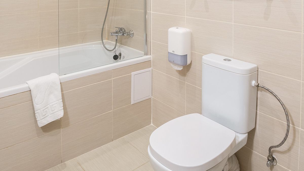A bathroom with a bathtub, toilet, and hand soap dispenser.