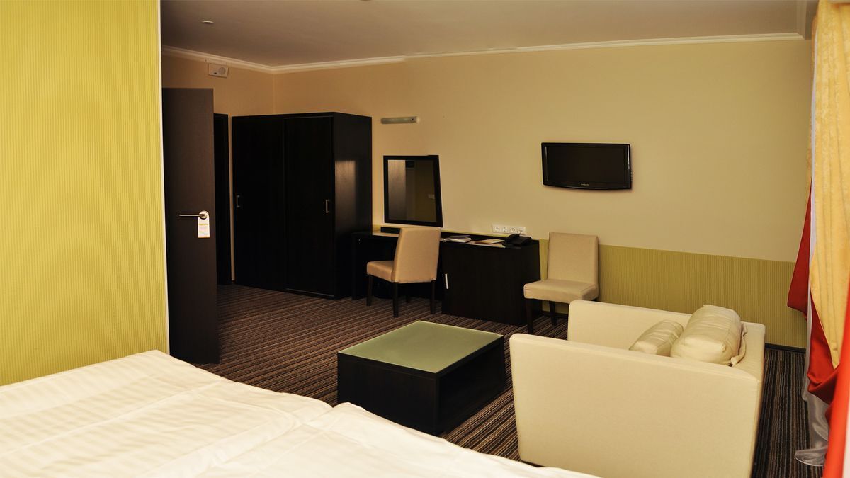 A hotel room with a bed, a desk, a chair, a television, and a small table.