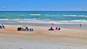 A beach with rows of beach chairs and umbrellas, a person sitting under a red umbrella, and the ocean in the background.