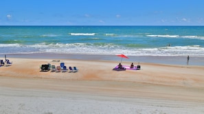A beach with rows of beach chairs and umbrellas, a person sitting under a red umbrella, and the ocean in the background.