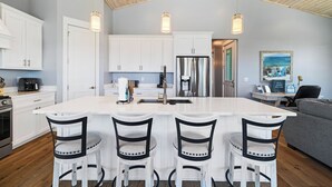 A modern kitchen with white cabinets, a large island with bar stools, stainless steel appliances, and pendant lighting. - Island Time Hers by Liquid Life (Gulf Shores)