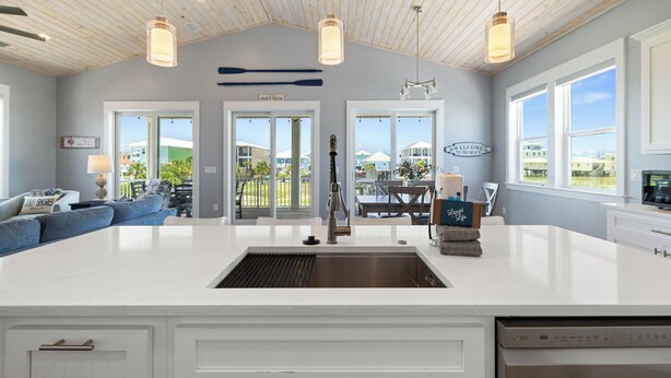 A spacious kitchen with a large island, white cabinetry, and a view of the beach through the windows. - Island Time Hers by Liquid Life (Gulf Shores)