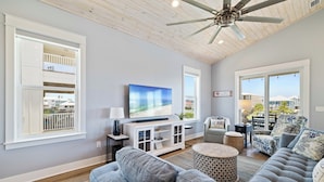 A spacious living room with a large flat-screen TV, a ceiling fan, and a view of the outside balcony. - Island Time Hers by Liquid Life (Gulf Shores)