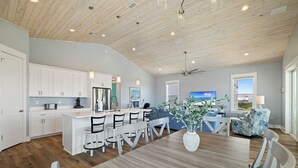A modern kitchen with white cabinets, a wooden island, and a dining area with a wooden table and chairs. - Island Time Hers by Liquid Life (Gulf Shores)