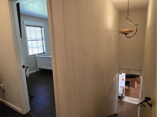 A hallway with a door leading to a room with a window and a radiator. There is a small staircase leading to another room.