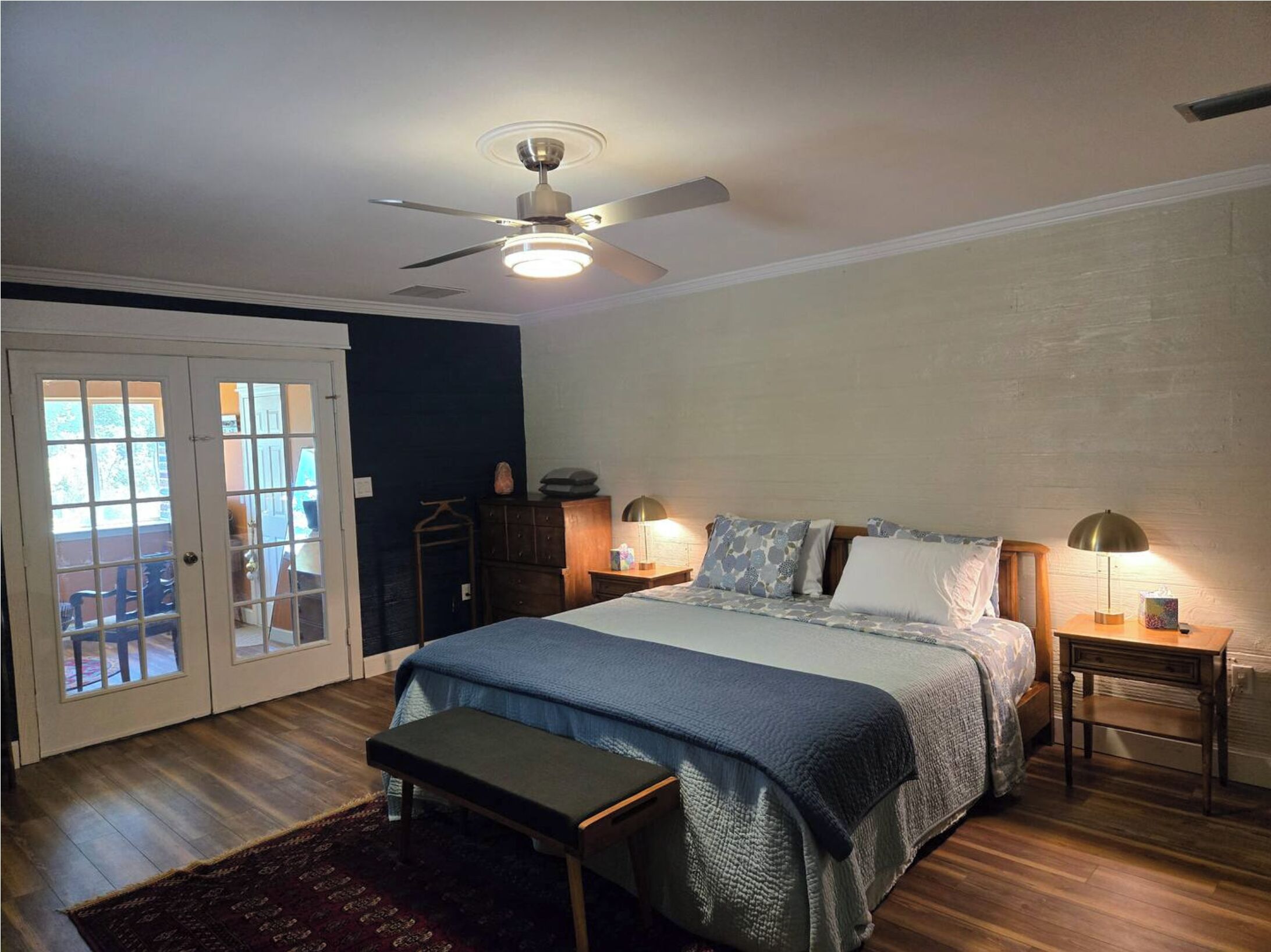 A bedroom with a bed, a bench, a ceiling fan, and two bedside lamps.