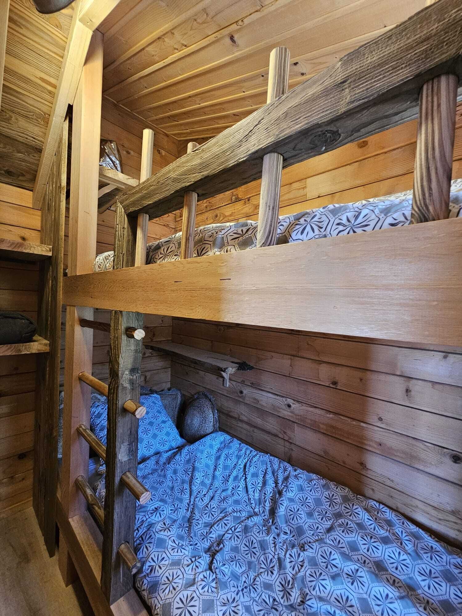 Ein Stockbett mit einer Leiter, Holzwänden und gemusterten Bettbezügen.