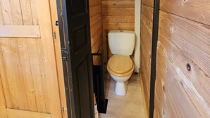 Een kleine badkamer met houten lambrisering, een toilet en een deur naar een andere kamer.